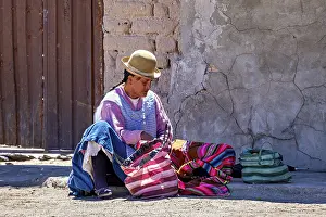 Typical: Man in traditional dress sits on the floor and sorts colourful bags on a wall