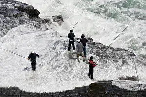 Muriwai: Men fishing on rock outcrop amidst breaking waves
