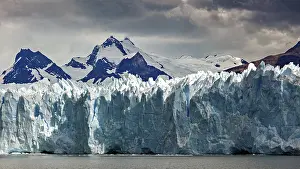 Glaciers: Mighty glacier landscape against a dark sky and snow-capped mountains in the background