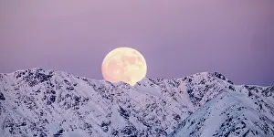 Moonlight: full moon rising into a pink sky in a winter mountain