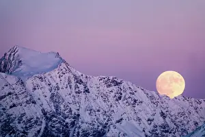 Moonlight: full moon rising into a pink sky in a winter mountain