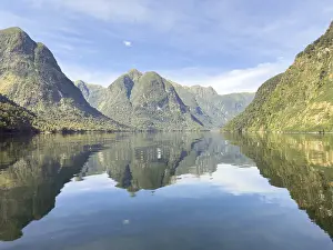 Estuary: Mountains with reflections in the water against a blue sky in Doubtful Sound