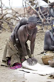 Preparing: Mursi people - woman preparing food with baby sleeping