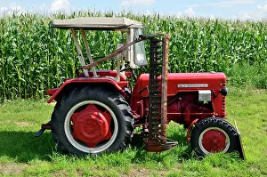 Singly: Old tractor with mower in front of a maize field