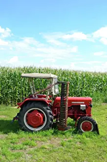 Singly: Old tractor with mower in front of a maize field