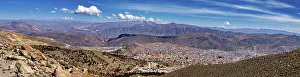 Cities: Panoramic view over a city in a wide valley with surrounding mountains under a cloudy sky