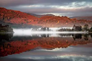 Cumbria: Reflecting water surface at sunrise with fog, hilly