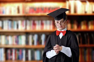 Board: Schoolboy wearing a graduation cap in a library