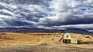 Home: A small house in an open, rural landscape under a dramatically cloudy sky