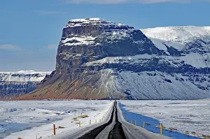 Leading: Straight, snow-covered road leading towards a mountain
