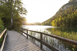 Lights: Sunrise in summer at Lake Thumsee near Bad Reichenhall with a wooden footbridge and a sun star over the lake
