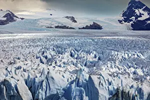 Glaciers: A vast icy landscape stretches out in front of a cloudy sky and majestic mountain peaks