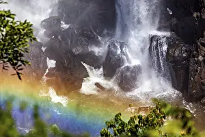 Waterfalls: Waterfall meets dark rocks, a rainbow shines in the foreground
