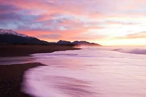 Beneath: Waves cover a black sand beach beneath snow covered mountain