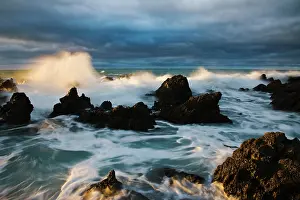 Crash: Waves crash under dramatic sky over rocky coastline at sunri