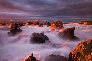 Crash: Waves crash under dramatic sky over rocky coastline at sunri