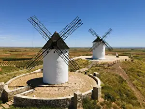 Wind: Two white windmills with black roofs on a hill surrounded