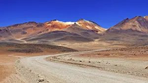 Roads: A winding sandy road through a dry landscape with reddish mountain peaks and blue skies