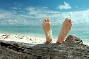 Destinations: Woman lying on the beach feet up on a tree trunk