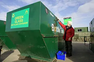 Bins: Woman recycling glass bottle into large green skip