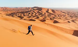 Merzouga: Woman running downhill, red sand dunes in the desert