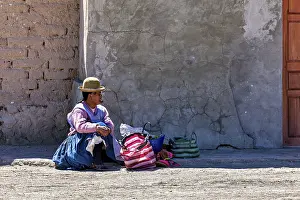 Typical: Woman in traditional dress sitting on the floor next to colourful bags in front of a wall