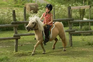 Minature: Young girl riding Shetland Pony in paddock