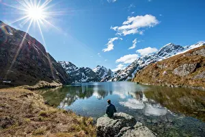 Westland: Young man sitting on a rock, mountains reflected