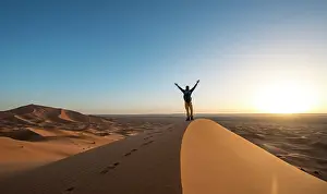 Merzouga: Young man stretches his arms into the air, sand