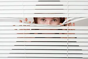 Model: Young woman looking curiously through blinds, Germany, E