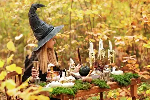 Scary: Young woman in witch costume sitting at table with