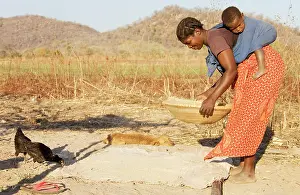 Mothes: Zambia - Tonga woman with child sifts grains near